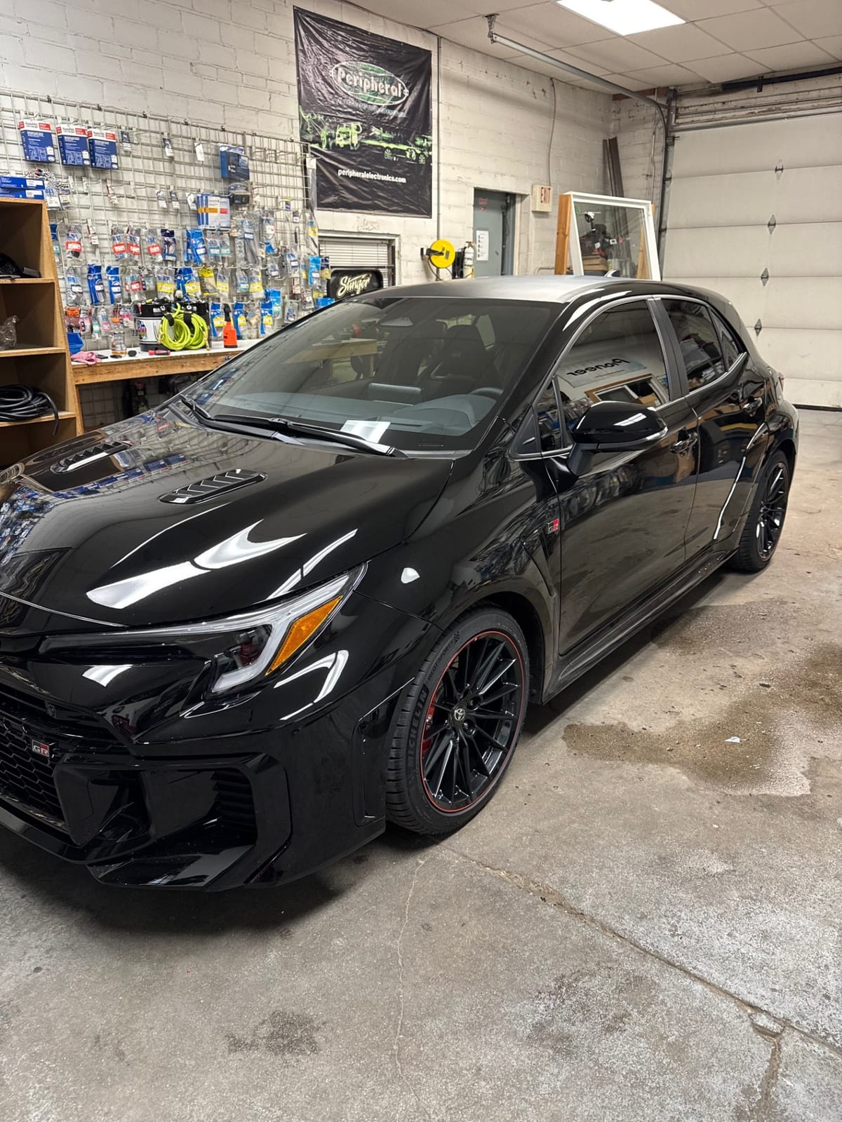 Black hatchback with dark side windows viewed from the front in a workshop.
