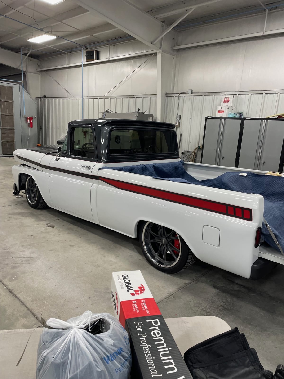 White and black classic pickup with a red side stripe, viewed from the rear in a workshop.